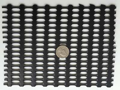 Black biaxial geogrid sample on the ground, and a coin is on the middle of it for contrast.