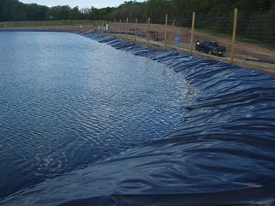 Black ECB geomembrane is laid around the artificial lake, and there is a wire mesh fence to protect the lake.