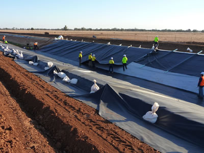 Some workers are working together to lay the black ECB geomembrane on the small slope.