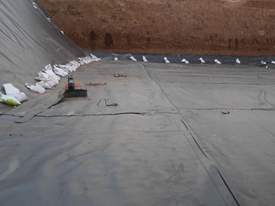 Black EVA geomembrane is laid around the whole landfill, and there is a machine and some cement bags on it.