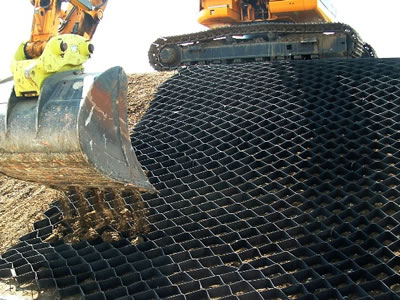 Black geocell is laid on the slope, and a excavating machine is filling the soil into it.