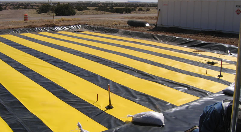 Black PVC geomembrane with some yellow strips is laid on the ground, and there is a person working on the black PVC geomembrane.