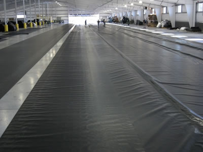 Black PVC geomembrane is laid on the ground in underground building, and there are some people working on it.