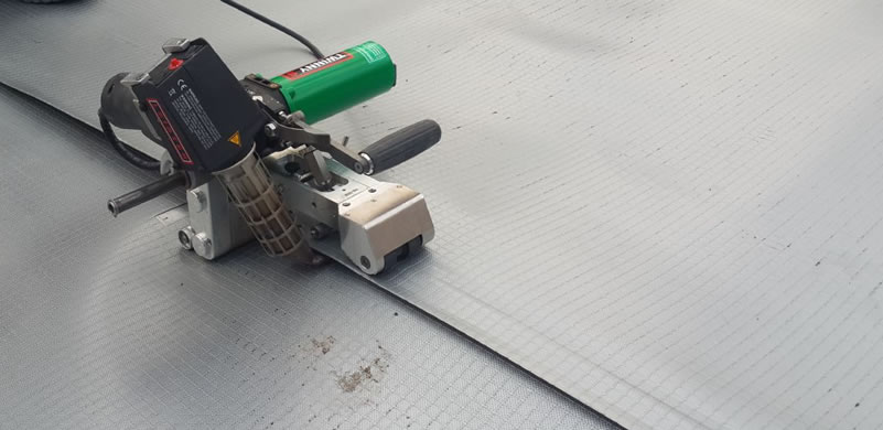 There is a person operating a small hot welding machine to stick the edges between two black ECB geomembranes.