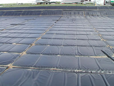 Black geomembrane liners is divided into neat rectangle pieces and covered on the ground, two aircraft are beside it.