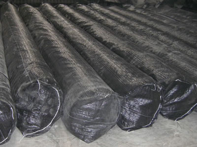 Some geosynthetic clay liner rolls are packaged with black woven bags lying on the ground.
