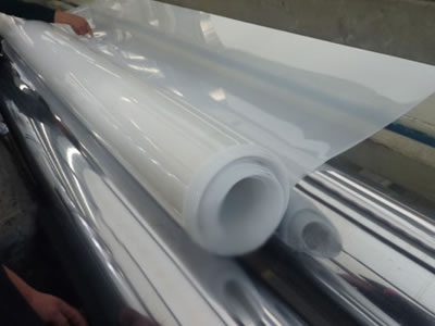 A roll of white LDPE geomembrane is winded by the production machine, and a hand is on it to test the quality.