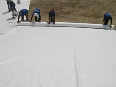 Some workers are laying the white long fiber geotextile fabric from the slope top to the bottom.