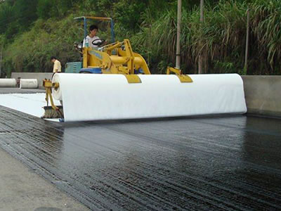 A person operates the machine to lay the short fiber geotextile fabric on the highway, and some rolls are behind it.