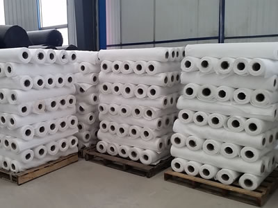 Numbers of white short fiber geotextile fabric rolls are piled up together orderly on wooden pallets.