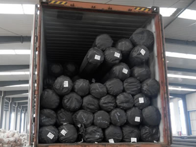 Short fiber geotextile fabric rolls packaged with black plastic film are on the truck waiting for transport.