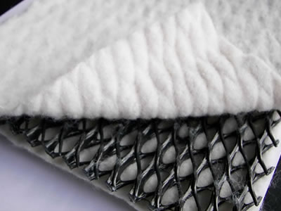 A piece of three dimensional composites drainage network sample with part white geotextile unfolded is lying on the ground.